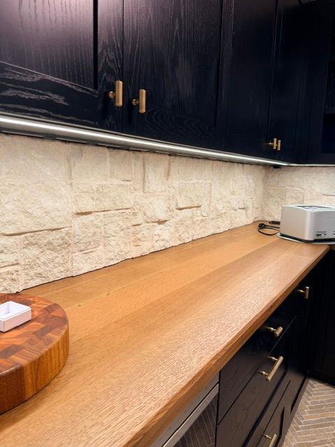 Wooden kitchen countertop with dark cabinets, stone backsplash, and a toaster oven on the right.
