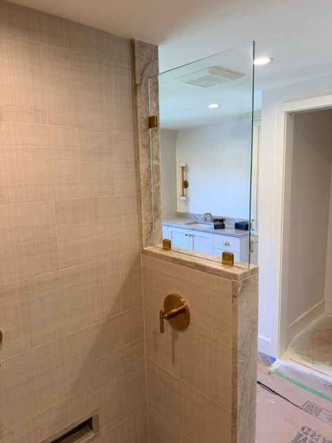 Bathroom shower with glass partition, beige tile walls, and a view into a bedroom or hallway beyond.