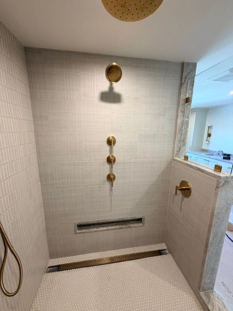 Tiled walk-in shower with brass fixtures, a handheld showerhead, and a built-in bench or ledge.