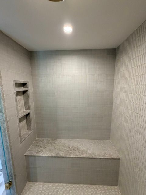 Small tiled shower or alcove with a built-in bench and recessed shelf, lit by a ceiling light.