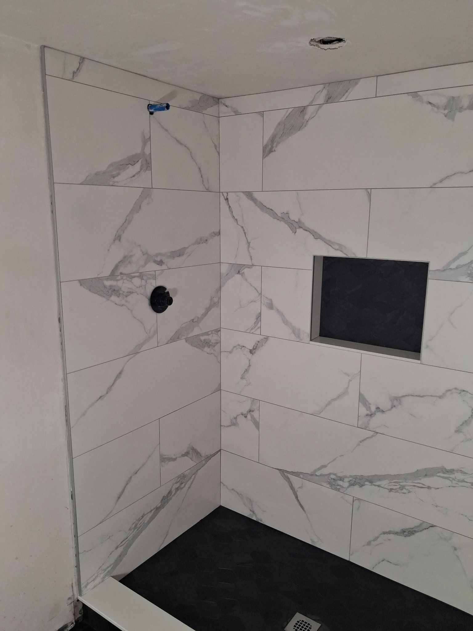 Modern tiled shower with black floor, wall niche, and round showerhead opening.