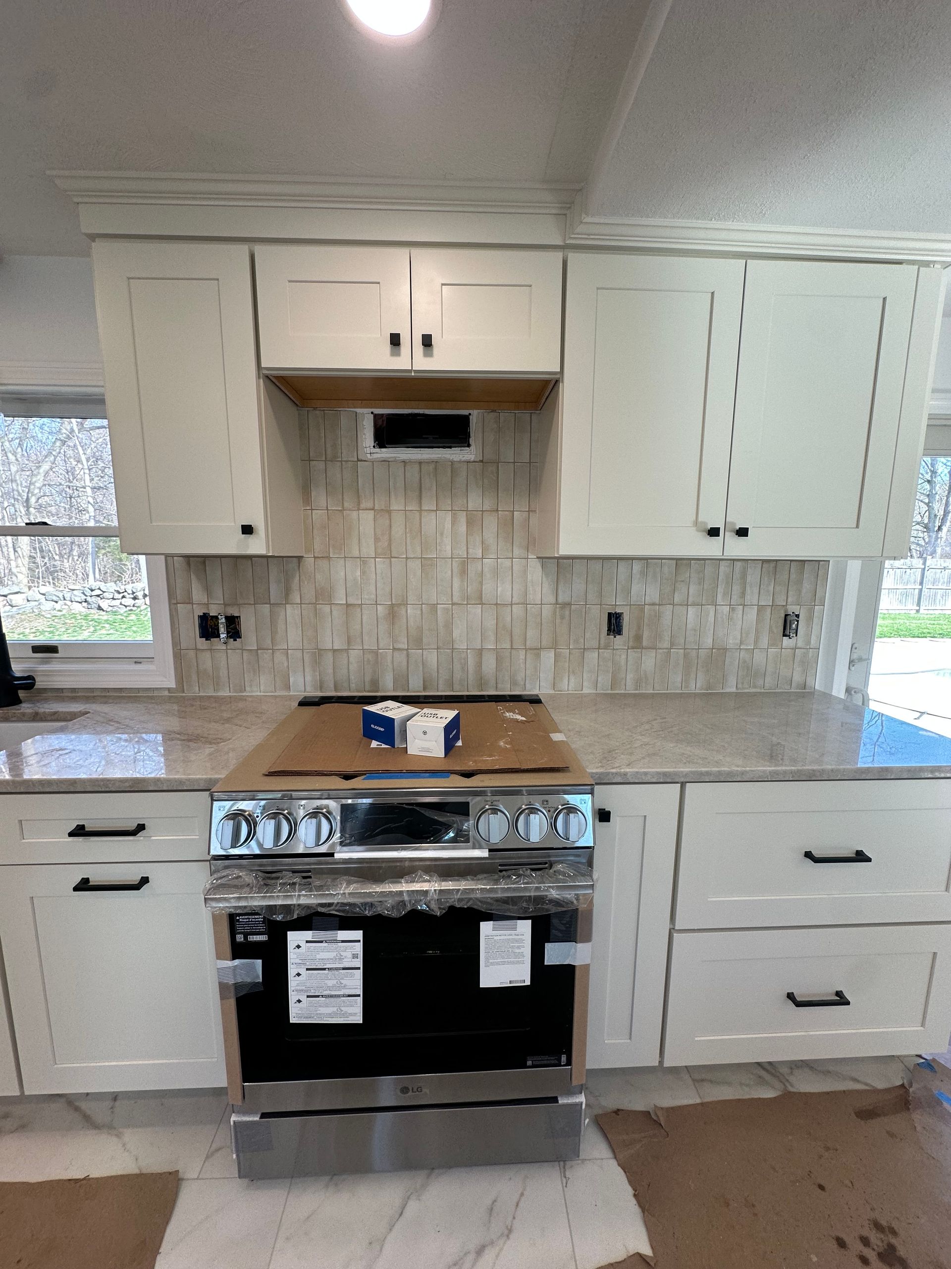 Bright kitchen with white cabinets, tiled backsplash, and a stainless steel stove under renovation.