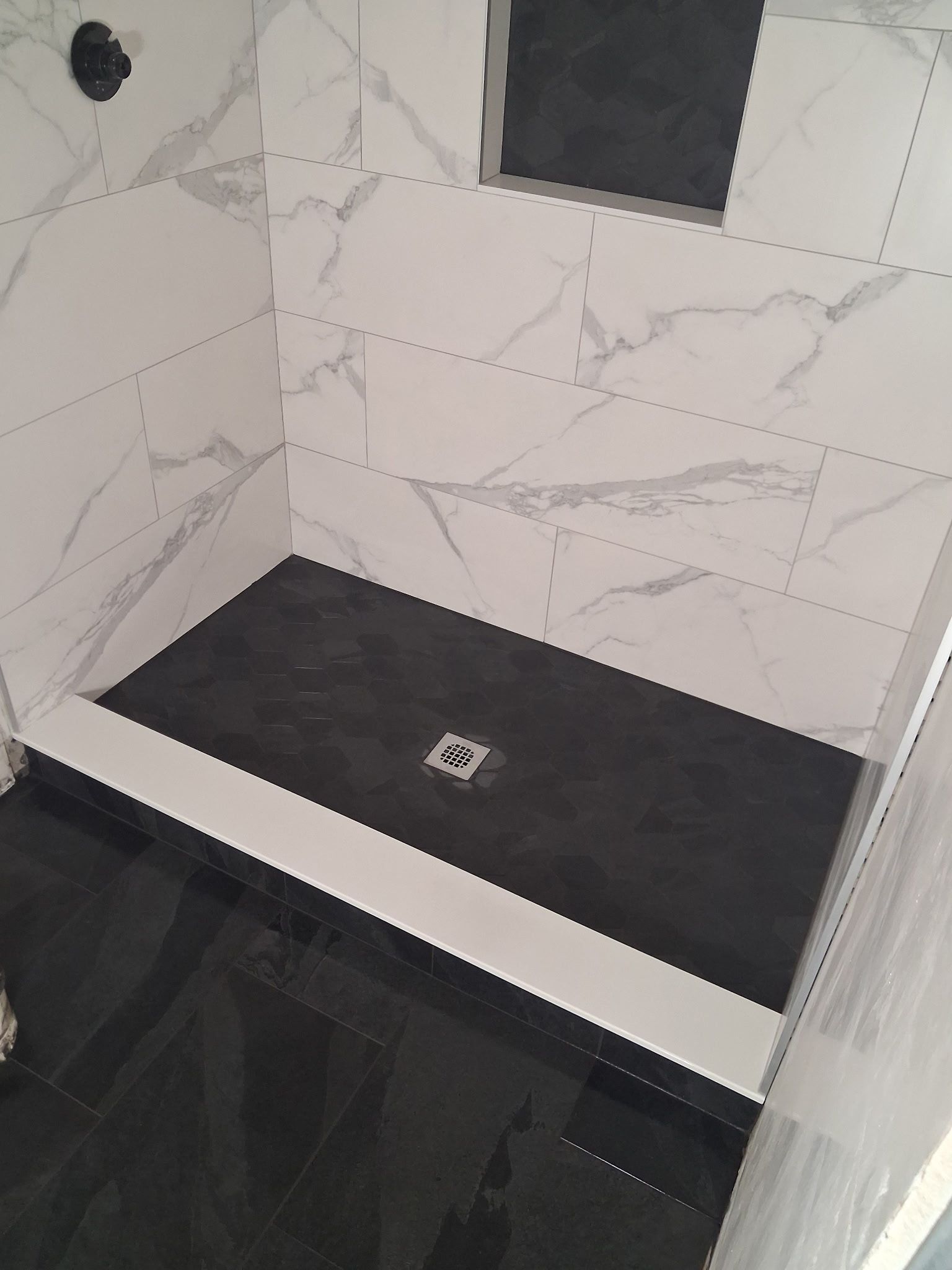 Modern shower stall with white marble-look walls, black floor, and center drain.