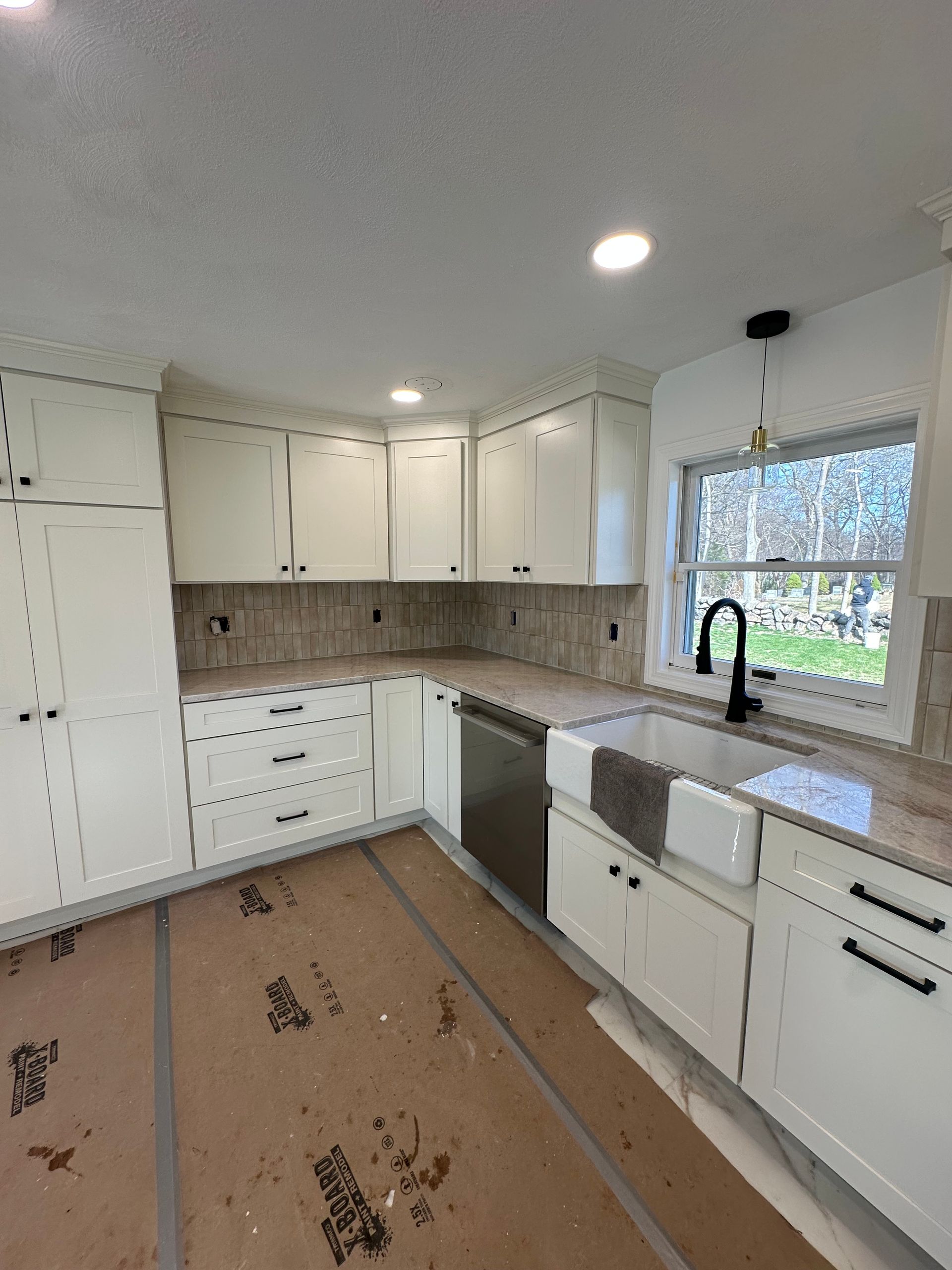 Bright white kitchen with U-shaped cabinets, window over sink, and unfinished floor covering.