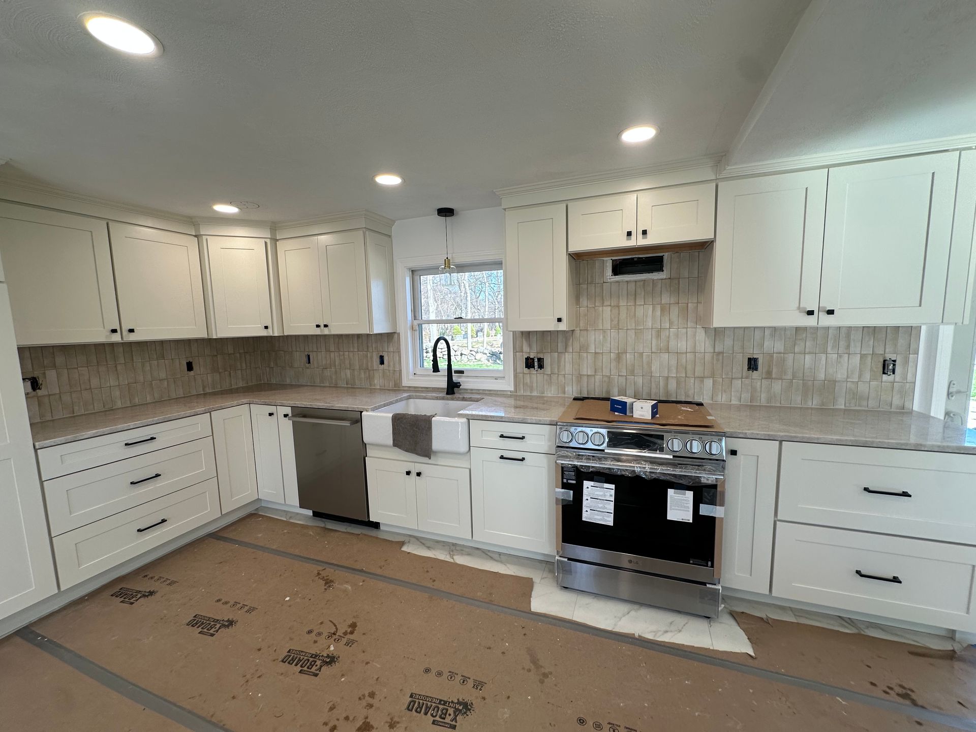 Bright new kitchen with white cabinets, beige tile backsplash, and protective floor covering during renovation