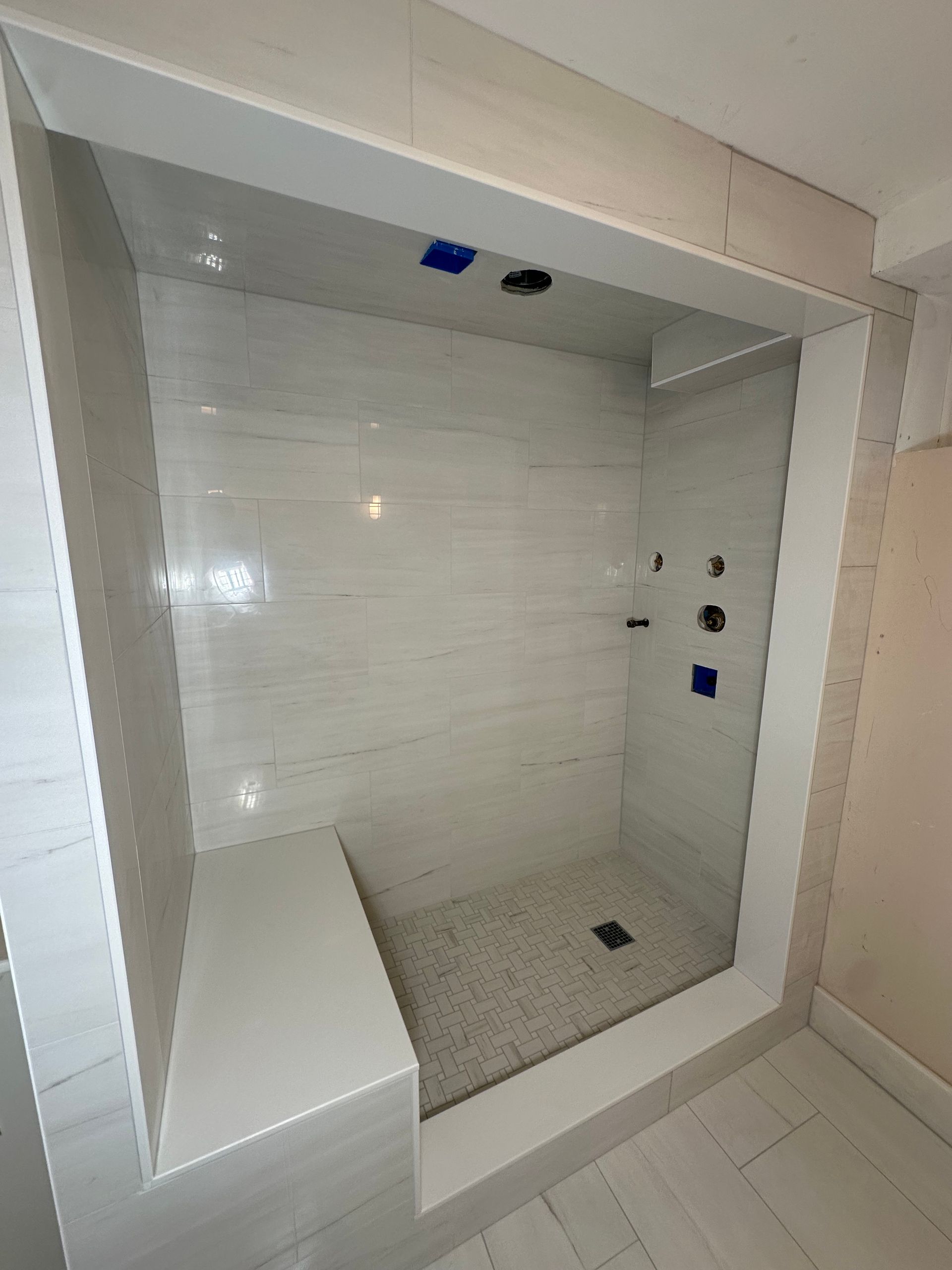 Empty tiled shower stall with built-in bench, wall controls, and drain in a bathroom