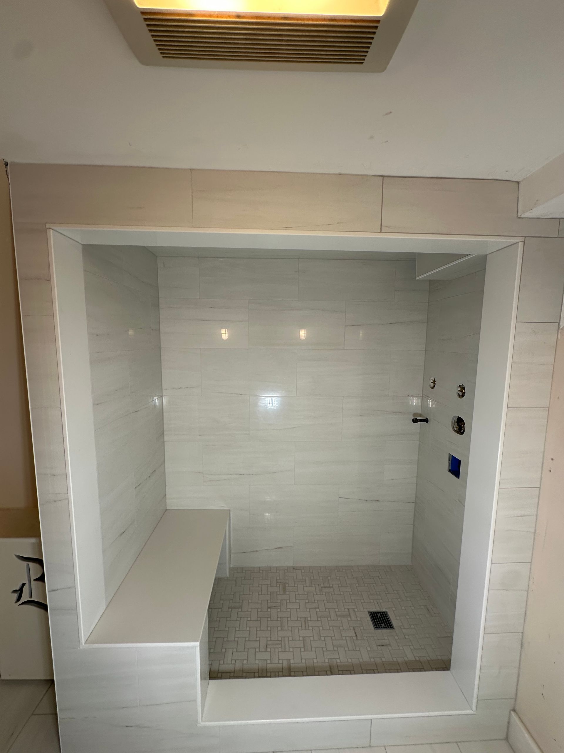 Empty white-tiled shower stall with built-in bench and small floor drain in a bathroom
