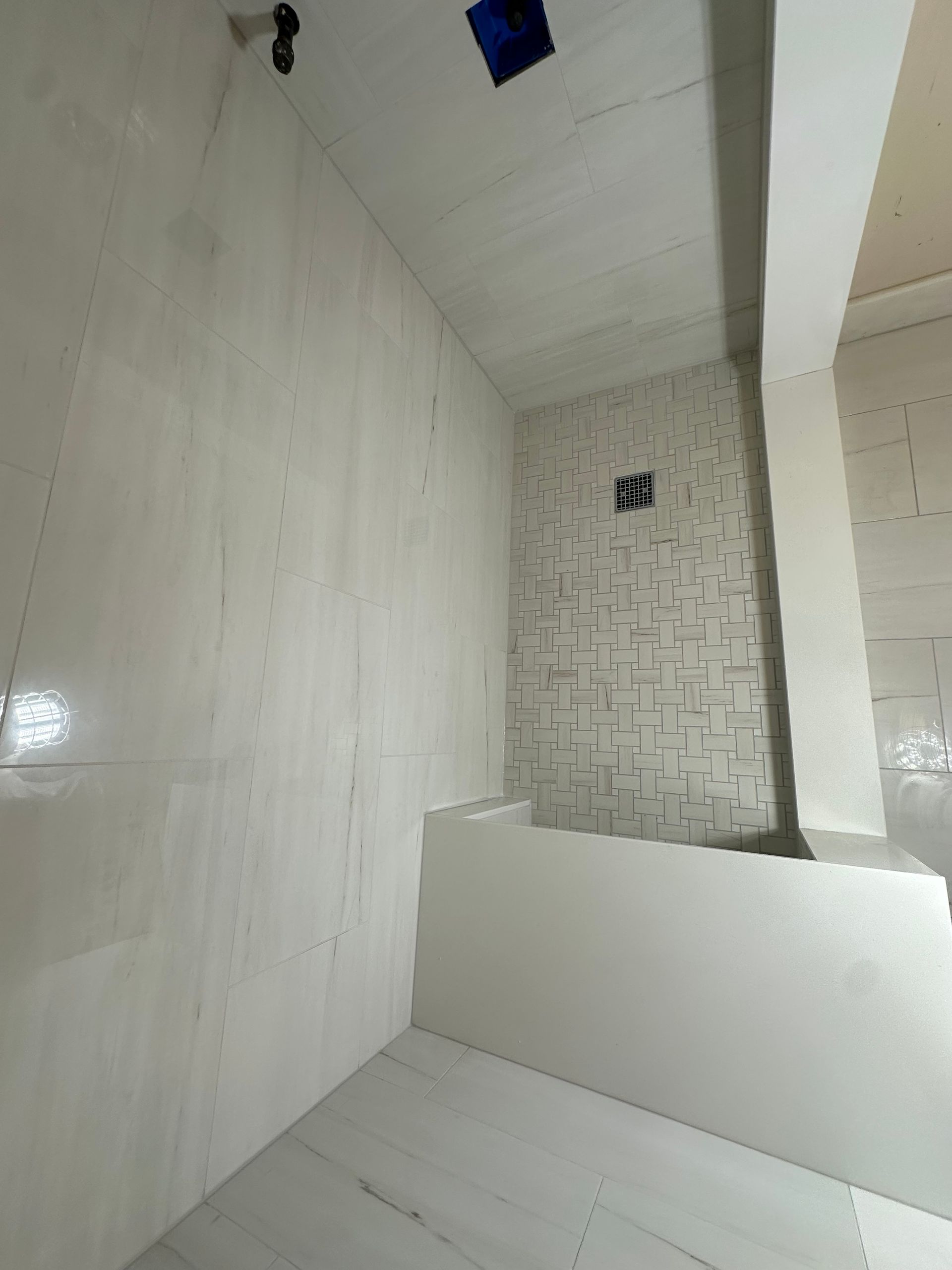 Bright white tiled bathroom or shower stall with a small blue fixture near the ceiling