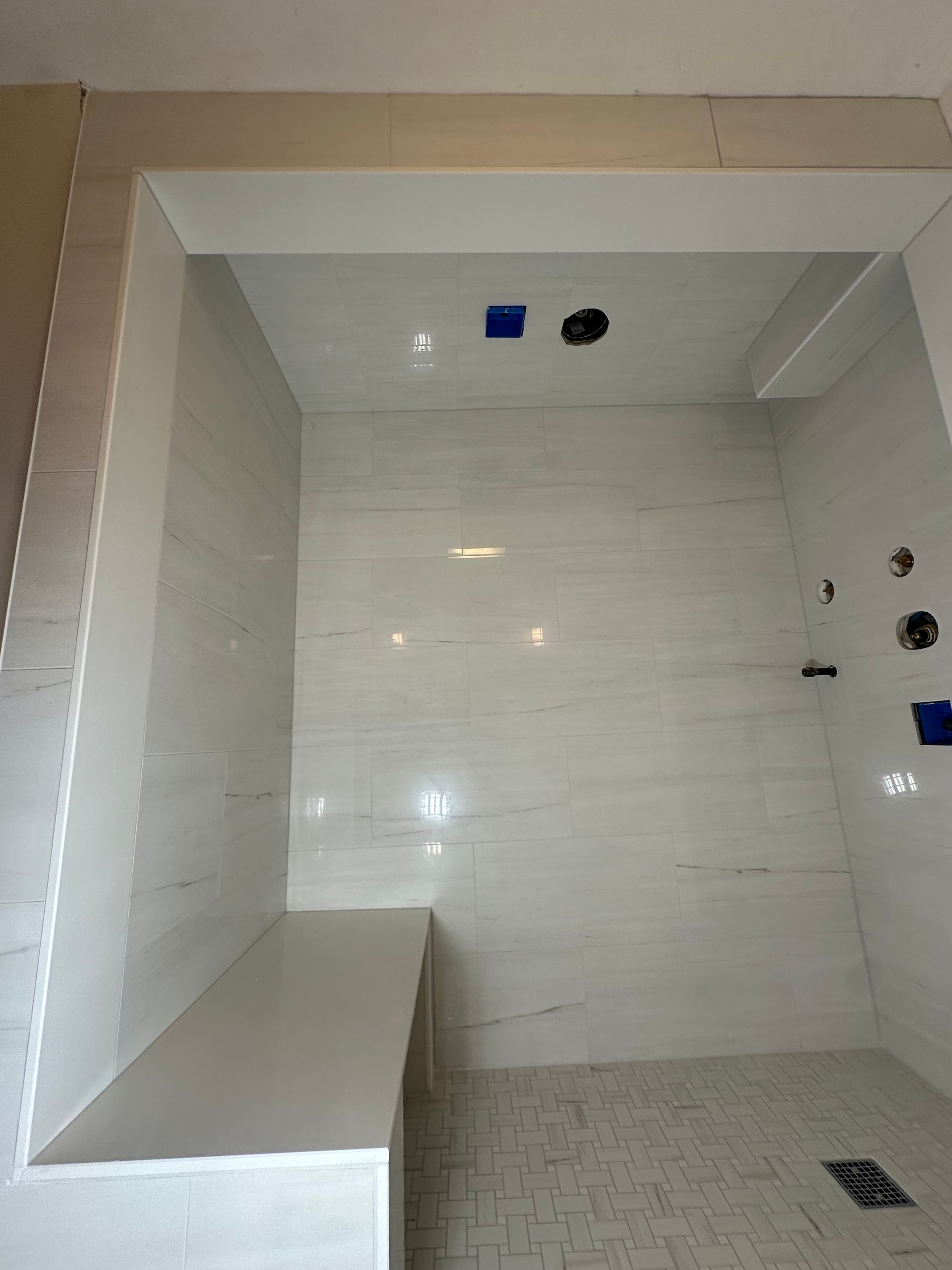 Empty tiled shower with built-in bench and wall fixtures, viewed from the doorway.