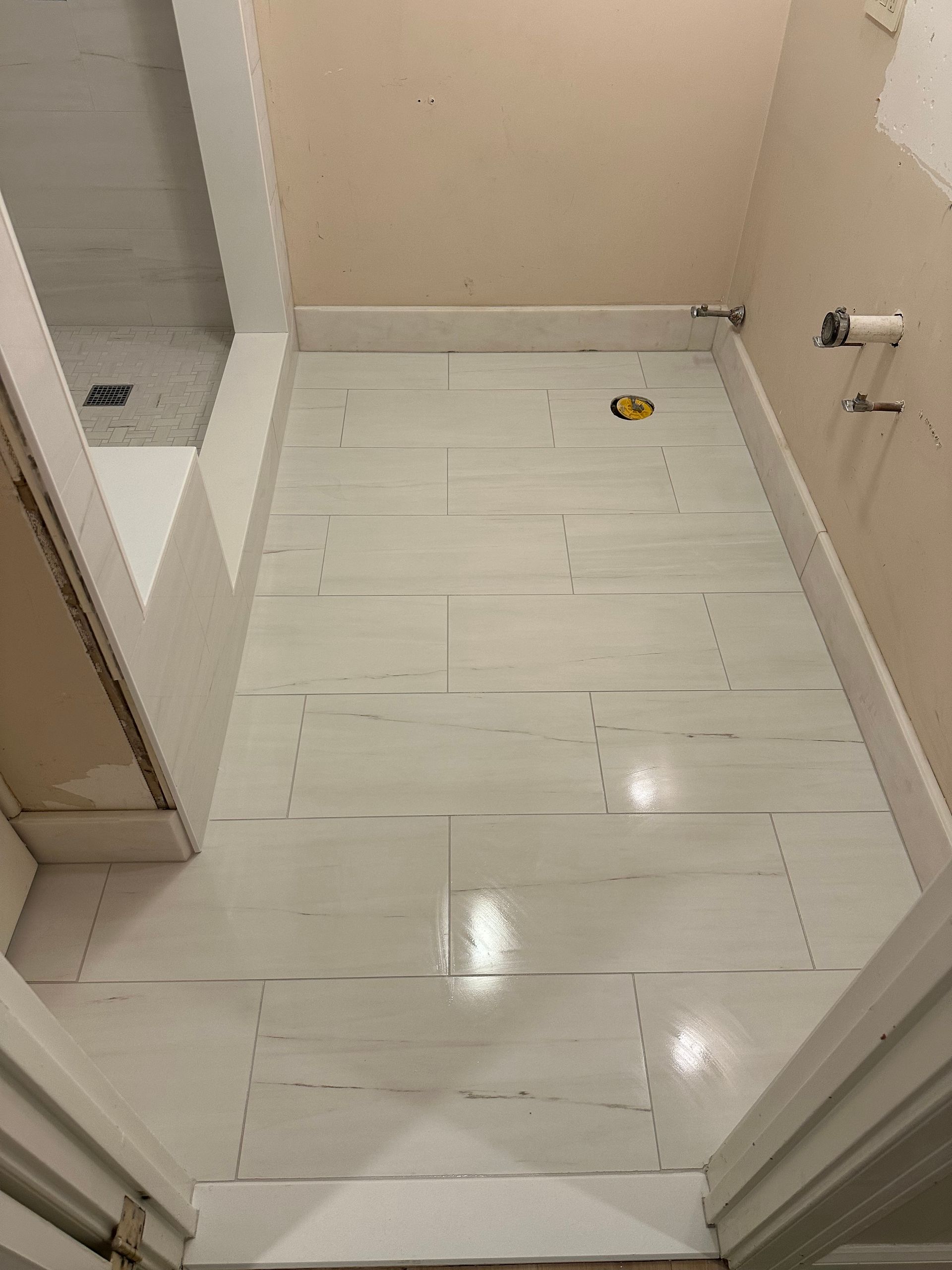 Small bathroom with white tile floor, beige walls, and a shower area on the left.