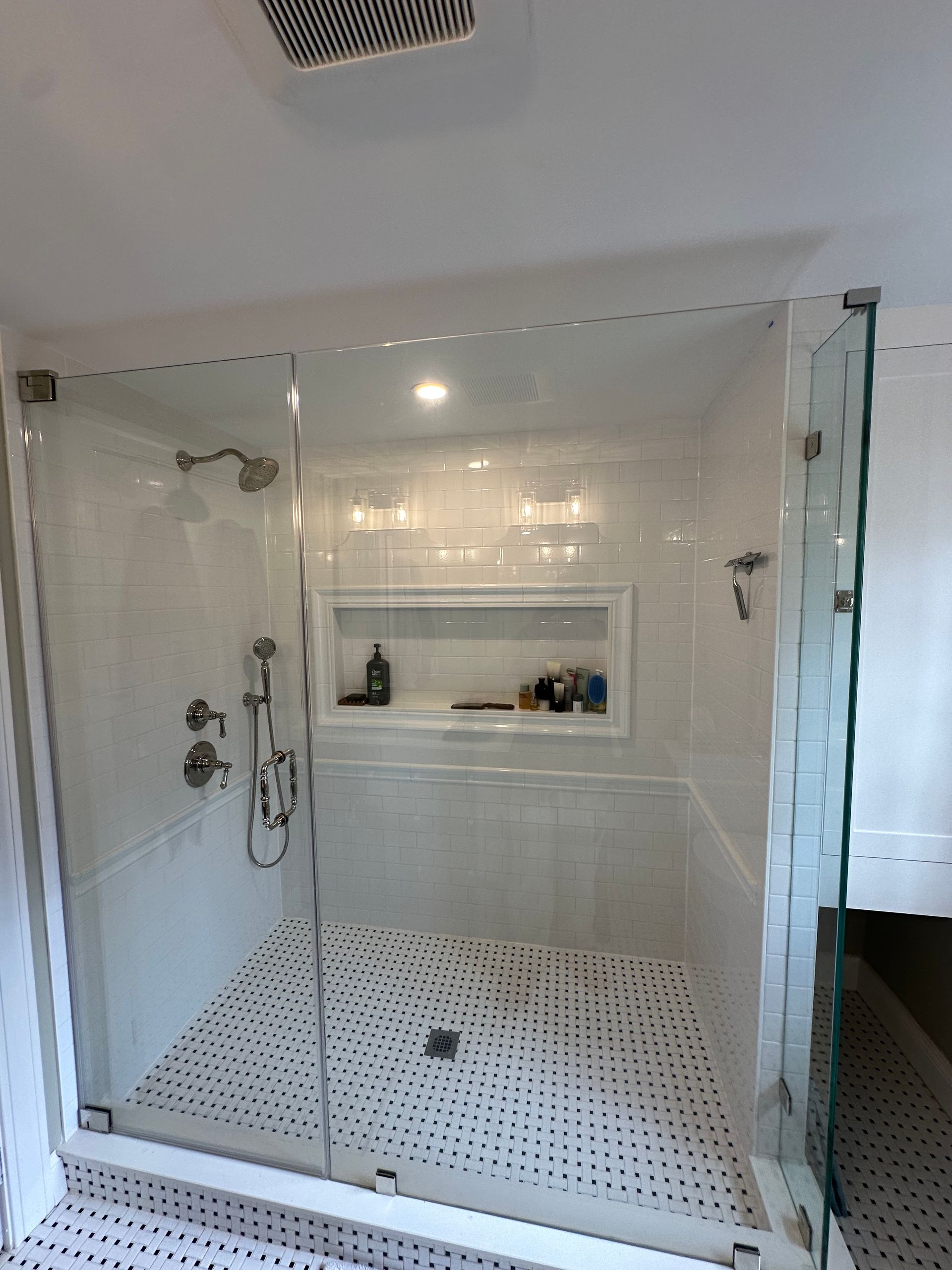 Modern glass shower with white tile, mosaic floor, and built-in shelf in a bright bathroom
