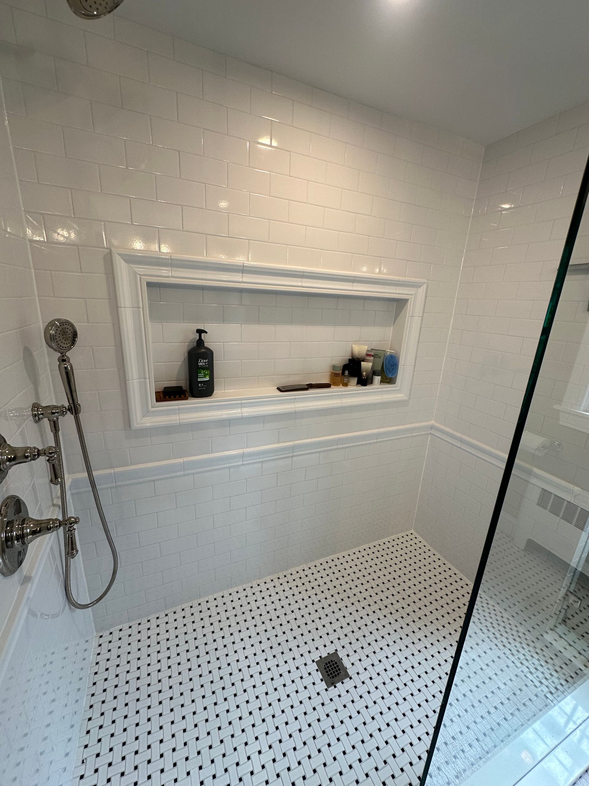 White tiled walk-in shower with a wall niche, handheld showerhead, and pebble-style shower floor.