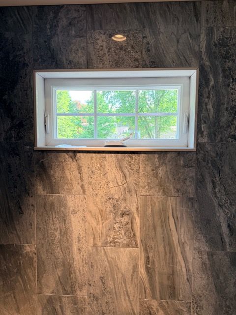 Small white-framed window set in a dark wood-paneled wall with light green trees outside.