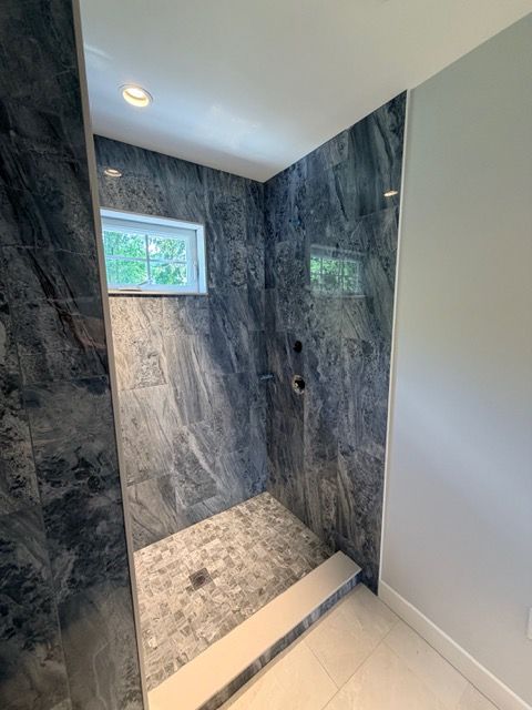 Modern tiled walk-in shower with dark stone walls, pebble floor, and a small window