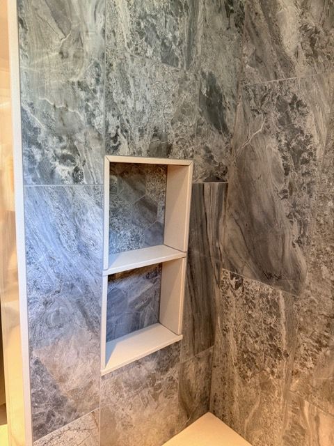 Built-in shower niche with two white shelves set in gray marble tile walls