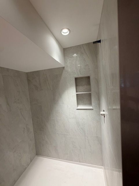 Small modern shower with gray marble-look walls, white floor, recessed light, and built-in niche.