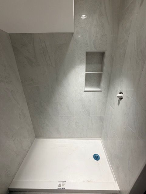 Empty tiled shower stall with built-in shelves, showerhead, and drain.