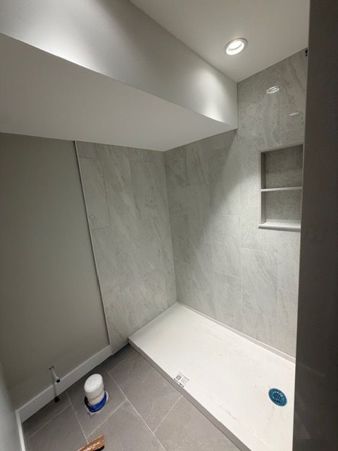 Small tiled shower under construction with gray marble-look walls, white floor pan, and recessed light above