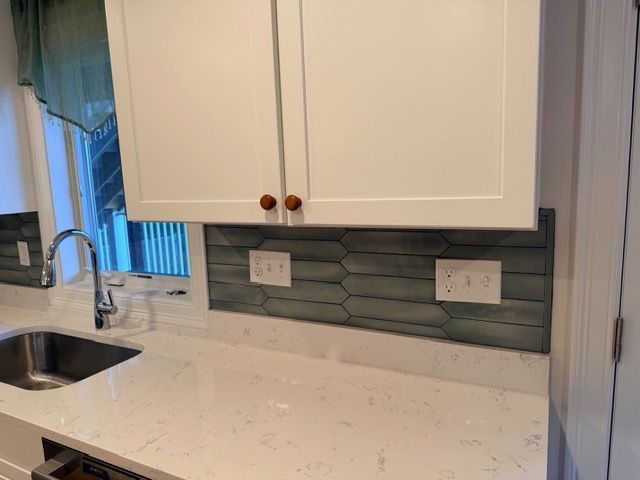 Kitchen counter with sink, white cabinets, gray backsplash, and a window