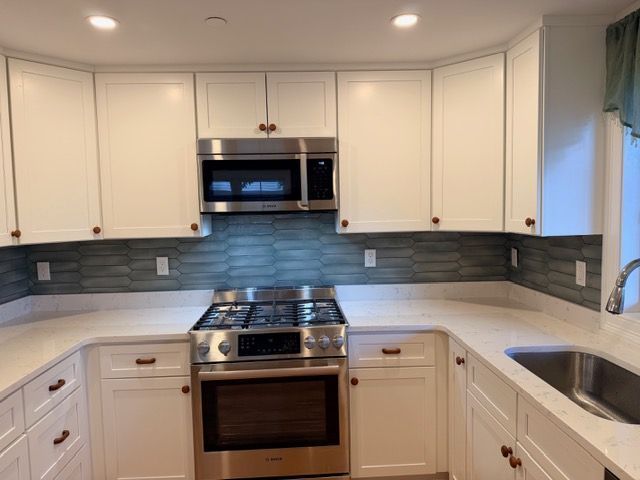 Modern white kitchen with stainless steel stove, microwave, and gray tile backsplash