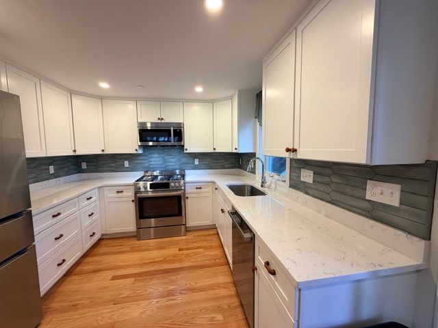 Bright modern kitchen with white cabinets, gray backsplash, stainless stove, and wood floors