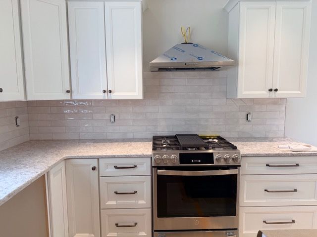 Modern white kitchen with cabinets, stainless stove, white tile backsplash, and granite countertops