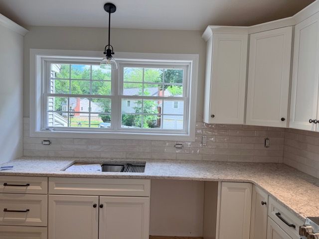 Bright kitchen with white cabinets, beige countertops, and a large window over the sink.