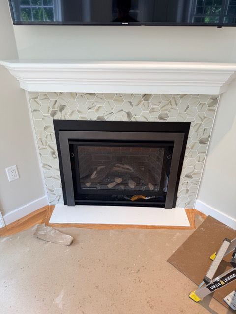 Corner fireplace with white mantel, patterned tile surround, and black glass front in a room under construction