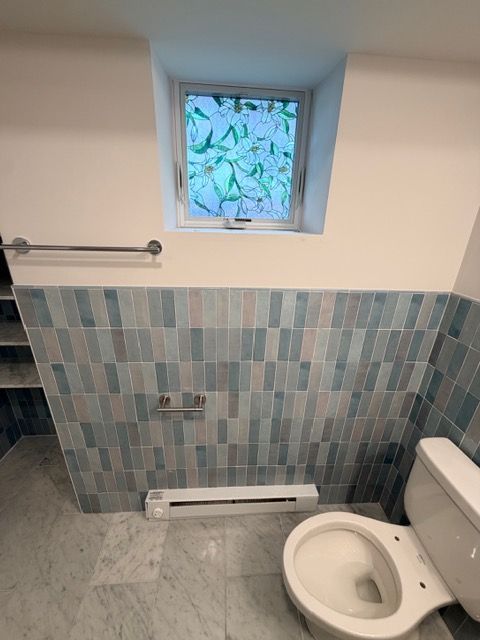Small bathroom with blue tile half-wall, frosted window, towel bar, radiator, and toilet.