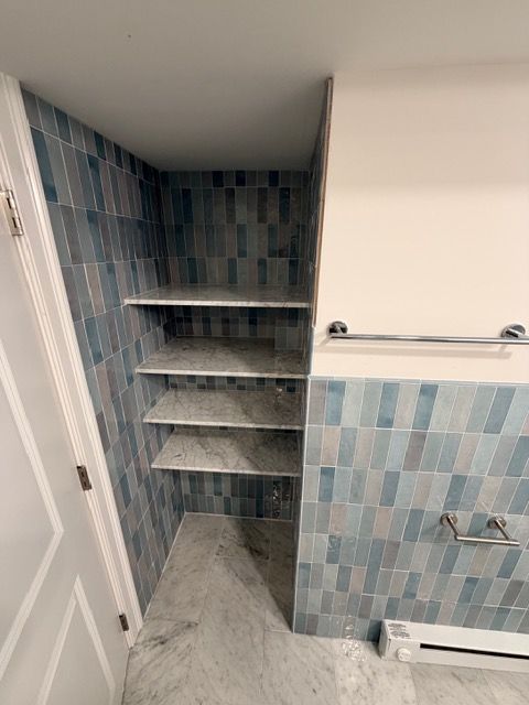 Small tiled bathroom with a shower nook, built-in corner shelves, and a towel bar.