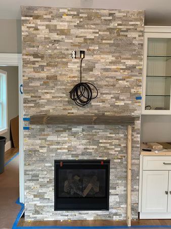 Stone fireplace with a mounted TV cable hanging above and a white cabinet beside it in a living room