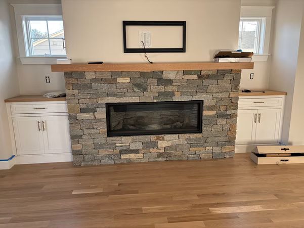 Living room with stone fireplace, white built-in cabinets, and hardwood floors