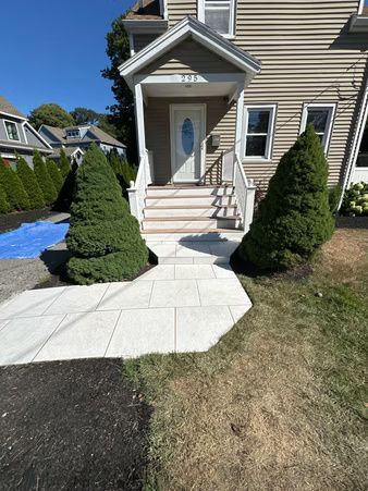 Front entrance of a beige house with white steps, potted shrubs, and a curved concrete walkway.