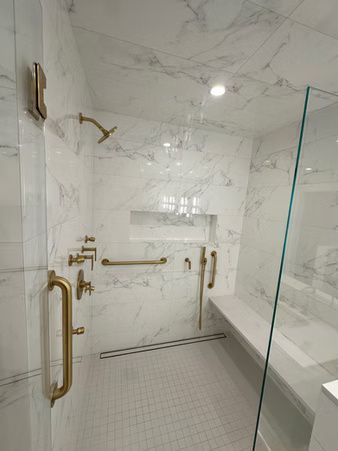 Accessible marble bathroom with grab bars, bench seat, and glass shower enclosure