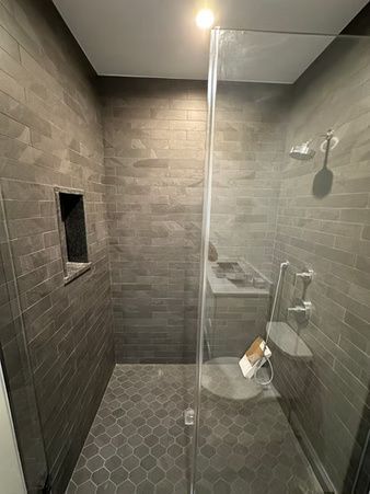 Modern gray-tiled walk-in shower with glass door, built-in niche, bench, and wall-mounted showerhead