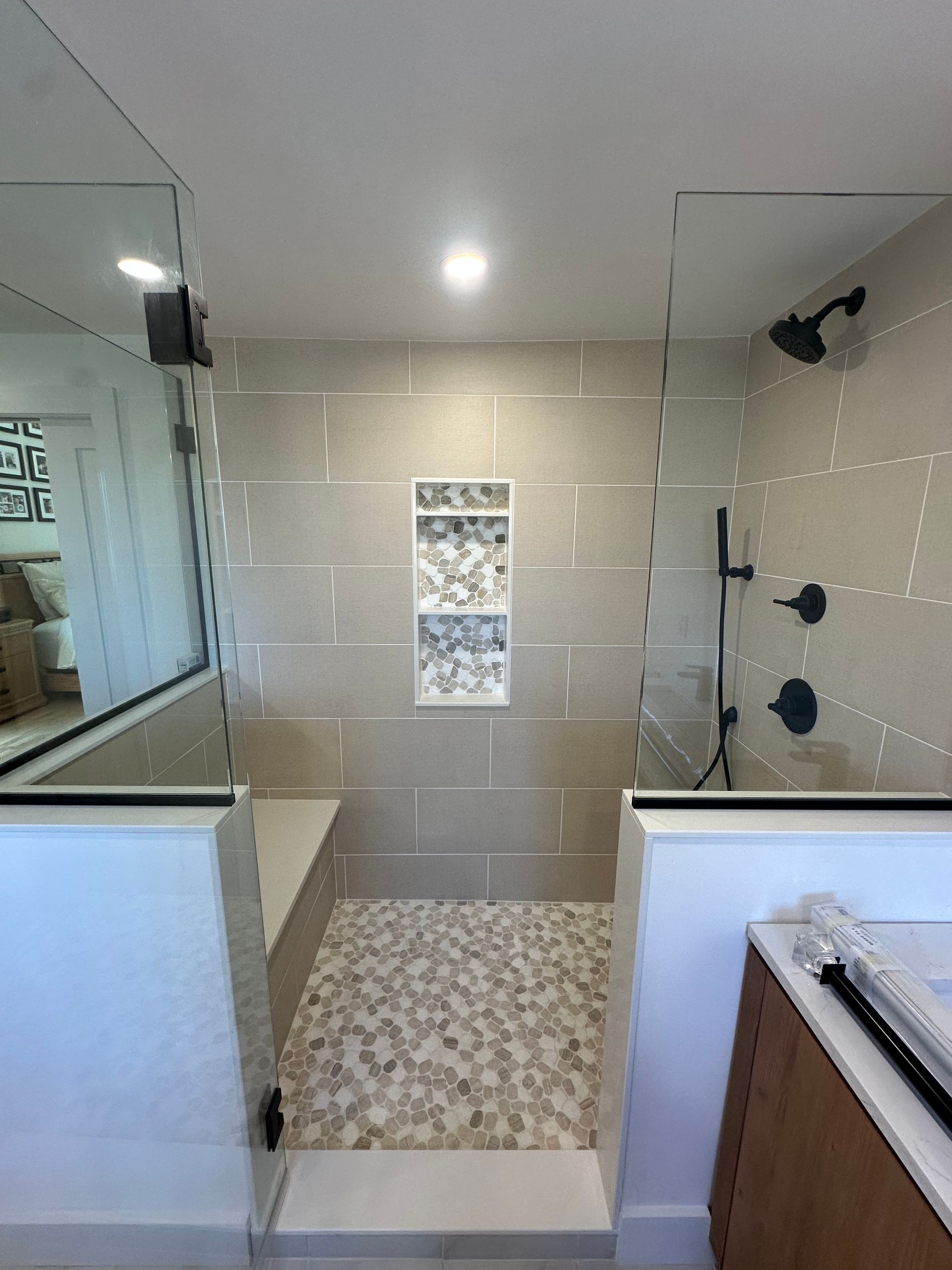 Modern bathroom shower with glass partitions, beige tile, and pebble mosaic floor.