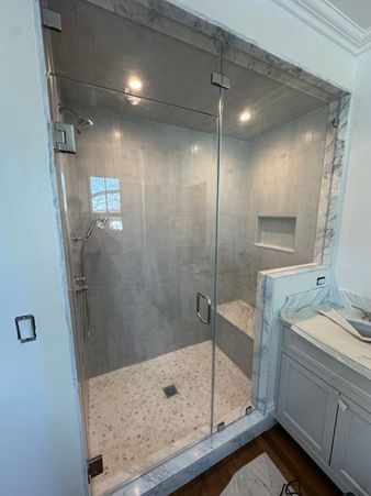 Glass-enclosed shower with gray tile walls, a bench, and a tiled floor beside a bathroom vanity.