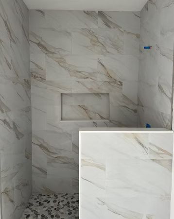 Small tiled shower alcove with marble-look walls, mosaic floor, and a recessed niche; close-up inset of wall tile.