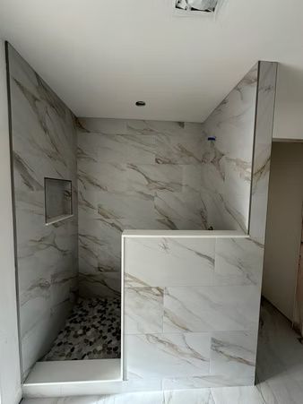 Marble-tiled walk-in shower with a built-in bench and recessed shelf, unfinished bathroom stall.