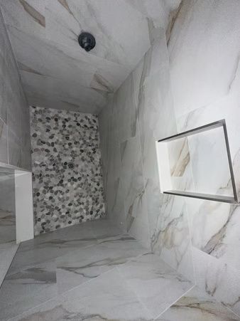 Empty marble-tiled shower stall with a mosaic accent wall and a small recessed shelf.