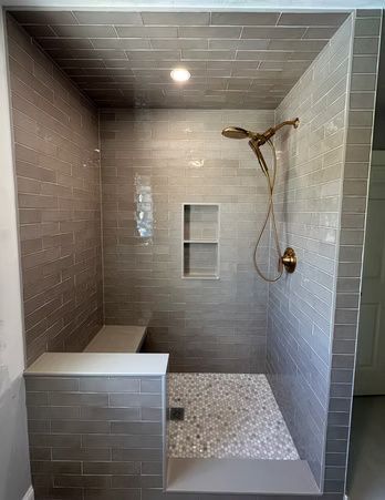 Modern tiled shower with built-in bench, niche, pebble floor, and brass showerhead.