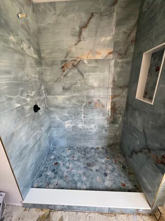 Empty tiled shower stall with gray walls, pebble floor, and a small window niche