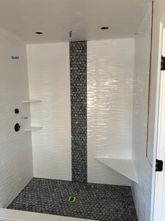 Modern white tiled shower with dark mosaic floor and built-in corner shelves