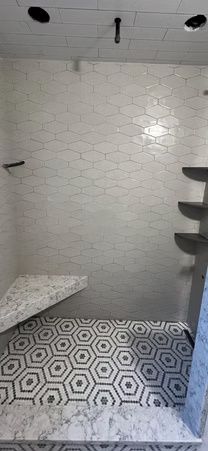 Modern shower stall with white tile walls and patterned floor, bench on the left, shelves on the right