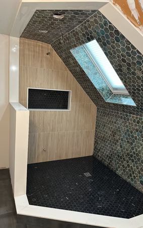 Modern shower stall with black hex tile, light wood paneling, and a skylight window.