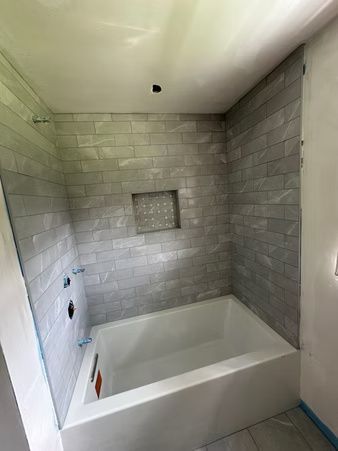 Tiled bathroom shower with white tub, gray walls, recessed niche, and ceiling light opening