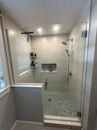 Modern walk-in shower with beige tile, glass door, rainfall showerhead, and built-in shelf niches