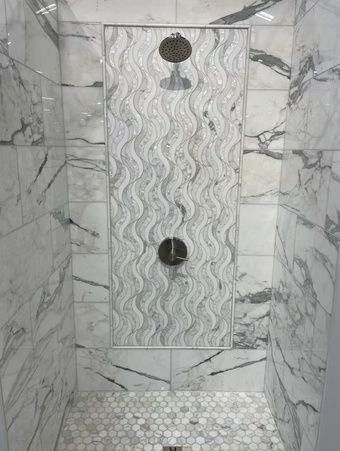 Tiled shower stall with marble-look walls, wavy accent panel, and two dark shower fixtures