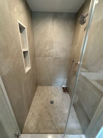 Empty tiled shower with glass door, built-in niche, and handheld showerhead.