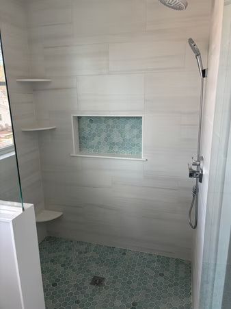 Modern shower with white tile, mosaic floor, built-in corner shelves, and handheld showerhead